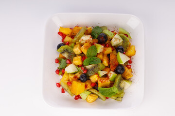 Mixed fruit salad arranged in a transparent rectangle tableware and garnished with mint leaf.