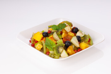 Mixed fruit salad arranged in a transparent rectangle tableware and garnished with mint leaf.