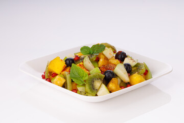 Mixed fruit salad arranged in a transparent rectangle tableware and garnished with mint leaf.