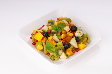 Mixed fruit salad arranged in a transparent rectangle tableware and garnished with mint leaf.