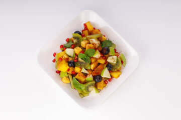 Mixed fruit salad arranged in a transparent rectangle tableware and garnished with mint leaf.