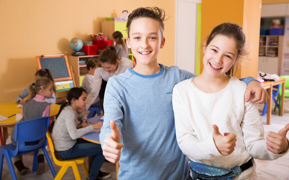 attractive boy and girl holding thumbs up, standing in class with kids