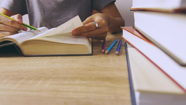 Close up and candid 4K of working woman who is reading a book concentratively on table with stacks of books as foreground shows concept of learning knowledge from self studying lifestyle. 