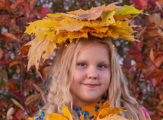 Autumn. Portrait of a girl with a wreath of yellow fallen maple leaves on her head in autumn colors. 