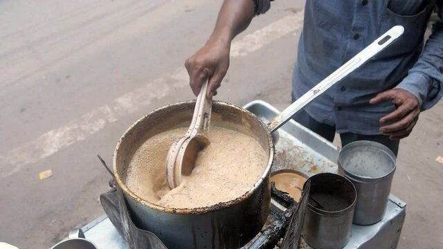 A tea vendor in casual clothes is busy preparing tea at a roadside tea stall. Tea with strong flavors / Kadak Chai being made on a roadside small Dhaba - refreshing drink  famous chaiwallah