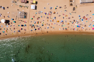 Birds eye view of beach with many people sunbathing on sand and swimming.