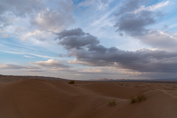 Nature and landscapes of dasht e lut or sahara desert with sand dunes in foreground and cloudy evening sky and mountain in background