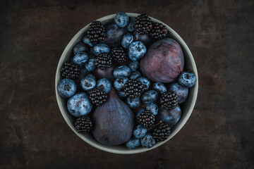 Dark berries and fruits in the bowl on the rustic background. Shot from above. Selective focus.