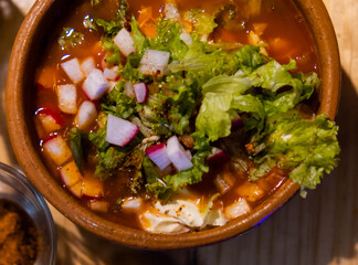 Clay bowl of delicious and traditional Mexican pozole on wooden table