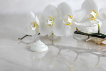 Obraz na płótnie Canvas texture of cosmetic cream on a marble background with white archidea flowers with reflection, beauty concept of natural cosmetics for face, body, hair care, spa services