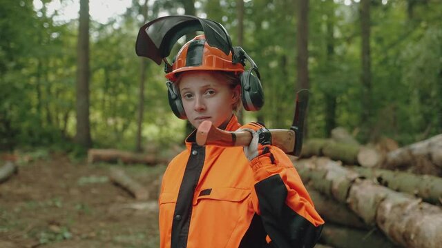 Portrait of a female logger standing in the forest,, a young specialist woman in protective gear holds an axe in her hands and works on deforestation, 4k slow motion.