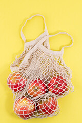 Fototapeta premium mesh shopping bag with organic apples fruit on yellow background. Caring for the environment.Zero waste concept. No plastic