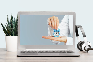 Laptop computer on desk. Doctors hands holding blue alarm clock on screen display. Time management...