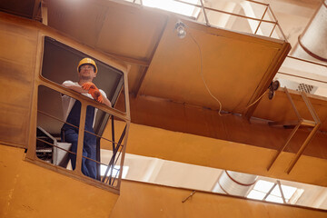 Handsome man builder sitting in operator cabin of overhead crane