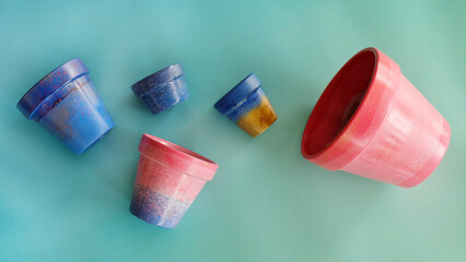 Flat lay of five colorful terracotta pots of different sizes. Painted in blue, pink and gold. 