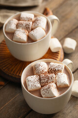 Cups of hot cocoa drink with marshmallows on wooden background, closeup