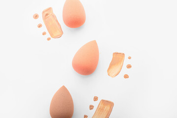Stylish makeup sponges and foundation samples on white background
