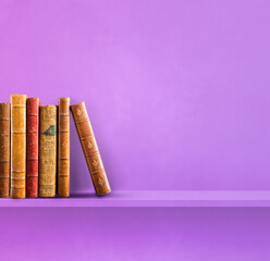 Row of old books on purple shelf. Square background