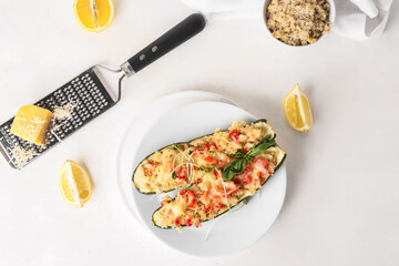 Plate with quinoa stuffed zucchini boats and ingredients on light background