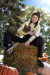 Teen girl with a dog sitting on a hay bale and pumpkins. Yorkshire terrier and model at the autumn harvest festival.