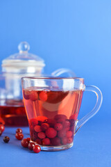 Glass cup of tasty cranberry tea on blue background, closeup