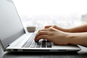 Female hands on laptop keyboard on a desk. Woman types on the laptop keyboard sitting near the window