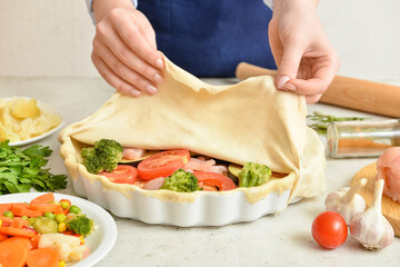 Woman preparing chicken pot pie with vegetables at kitchen table, closeup