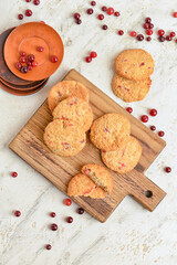 Wooden board with tasty cranberry cookies and berries on light background
