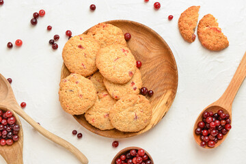 Wooden plate with tasty cranberry cookies and berries on light background