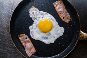 Delicious fried egg and bacon strips on a frying pan