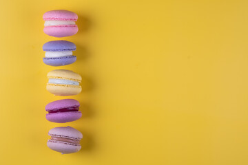Colorful composition of different varieties of macoron cookies on yellow background.