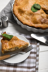 Baking dish and plate with piece of tasty chicken pot pie on white wooden background