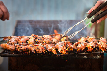 large pink shrimps langoustines with carapace lie on the grill with smoke. BBQ outdoor. Human hands...