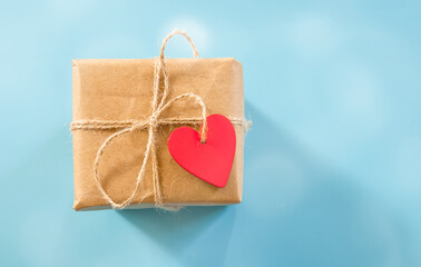 wrapped gift box with red heart shped tag over blue background, space for text, ad, promo, holidays greeting and celebration concept. 