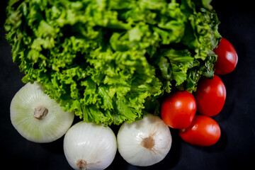 Tomatoes, onions, and big lettuce above black background