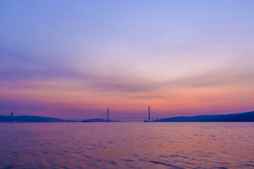 Russian bridge across the Eastern Bosphorus Strait in Vladivostok at dawn. The bright sea against the backdrop of a large automobile bridge.