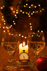 Old watch, two glasses of wine and a candle against the background of lights