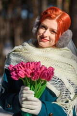 beautiful girl in a green coat and a wedding dress with a bouquet of flowers in the forest in winter