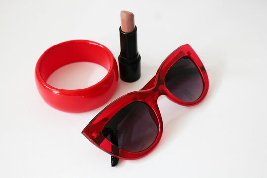 Women's lipstick, red sunglasses and a bracelet lie on a white background. Female accessories