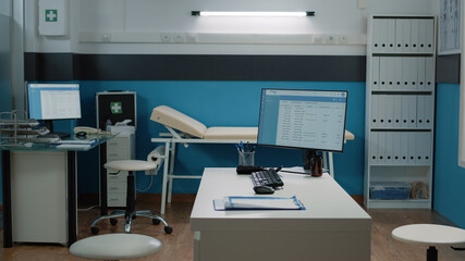 Empty doctors office with medical equipment and computer on desk at healthcare facility. Nobody in cabinet with documents and instruments for checkup and consultation. Space for examination