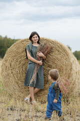 Naklejka na ściany i meble Beautiful young mother and cute son toddler are having fun on a haystack in the field 