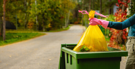 household waste - hand insert yellow plastic unsorted garbage bag into trash bin on the street....