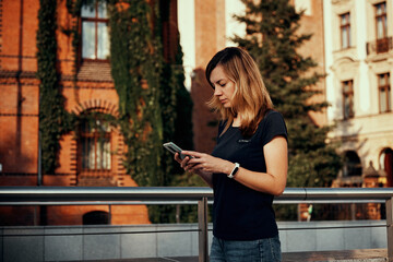 Woman using smartphone at city street. Millennial woman walks at city with mobile phone