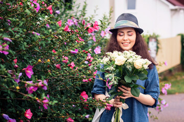 A smiling beautiful woman in a straw hat holds a bouquet of white roses and looks at him. Outside. The concept of March 8 and Mother's Day