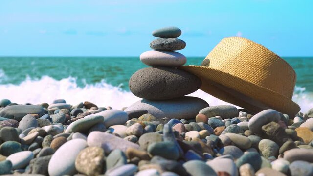 background for Zen meditation is balanced pyramid of stones stacked in close-up on sea beach. straw panama hat or hat, swinging in wind on pyramid of stones on beach against background of the sea.