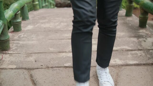 Legs in black pants and white sneakers walking on old bridge