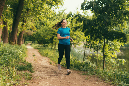 Cheerful woman is running alone in the forest near a lake.