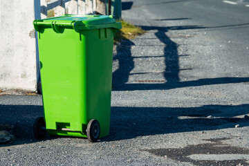 Green plastic wheelie bin in a street ready for collection, waste and recycle industry. Warm sunny day
