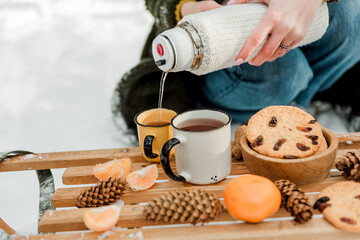 Winter picnic with tea, cookies, tangerines on a sled in a snowy forest. Green christmas wreath with pine cones