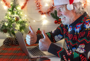 Fototapeta premium Old senior man happy in video call from home at Christmas. Using laptop gesturing optimistic smiling beard new year